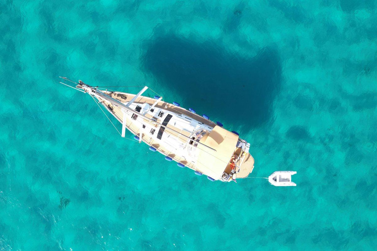 A sailing yacht and its tender at anchor in turquoise water off Porto Cervo, Costa Smeralda, Sardinia